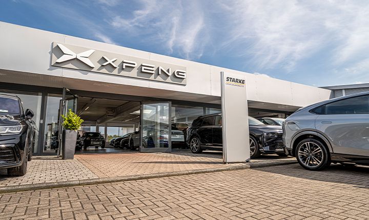 Das Bild zeigt den Eingang von unserem XPeng Standort. Über der Tür ist das XPeng Logo angebracht. An einem Schild daneben steht STARKE Automobilgruppe. Im Vordergrund ist der Hof mit verschiedenen Fahrzeug zu sehen.